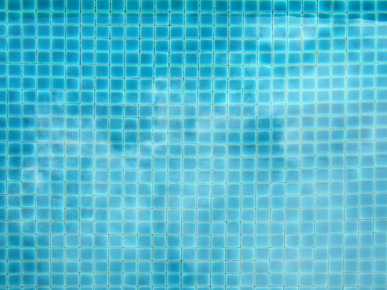 A detailed view of blue swimming pool tiles with a subtle wave pattern.