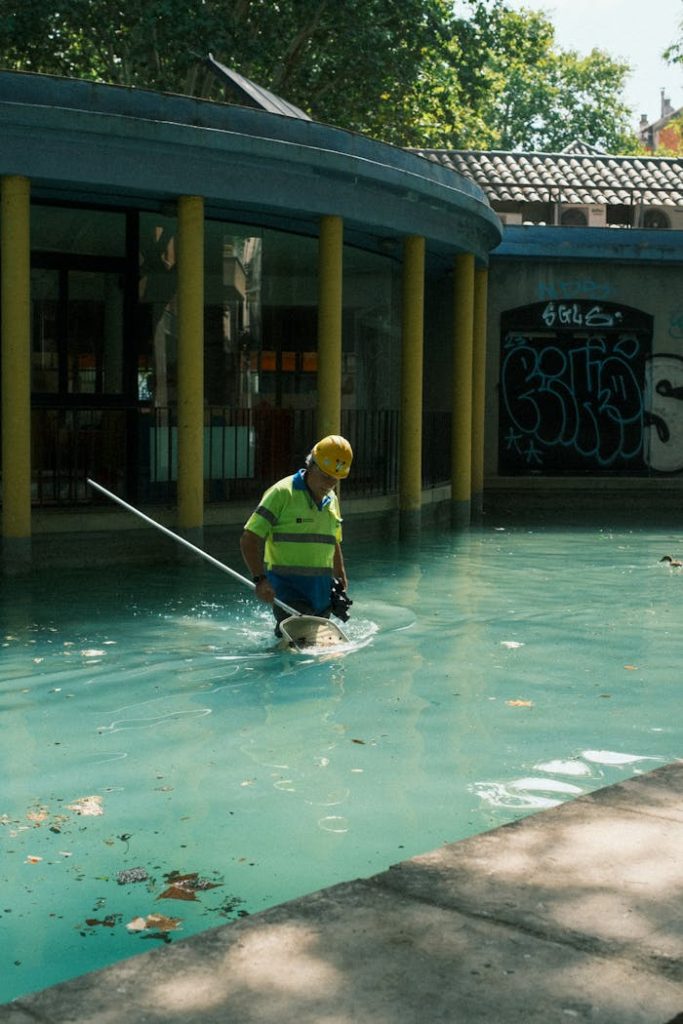 A pool maintenance worker wearing safety gear cleans an outdoor pool in Barcelona, Spain.